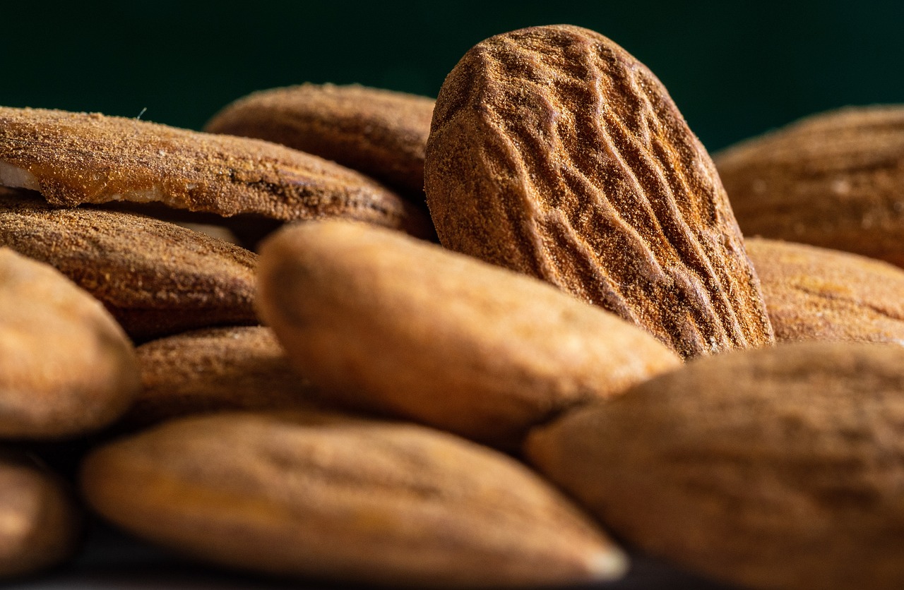 Close-up of several whole, unshelled almonds piled together, focusing on one almond with a textured outer shell.