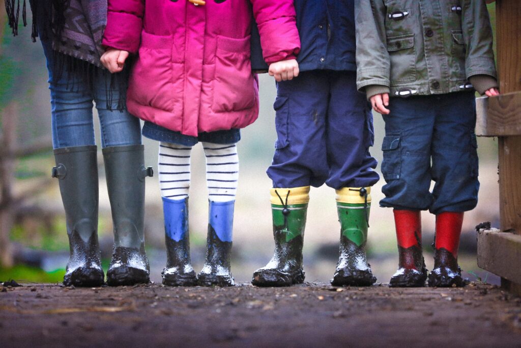 children from chest down wearing rainboots and holding hands