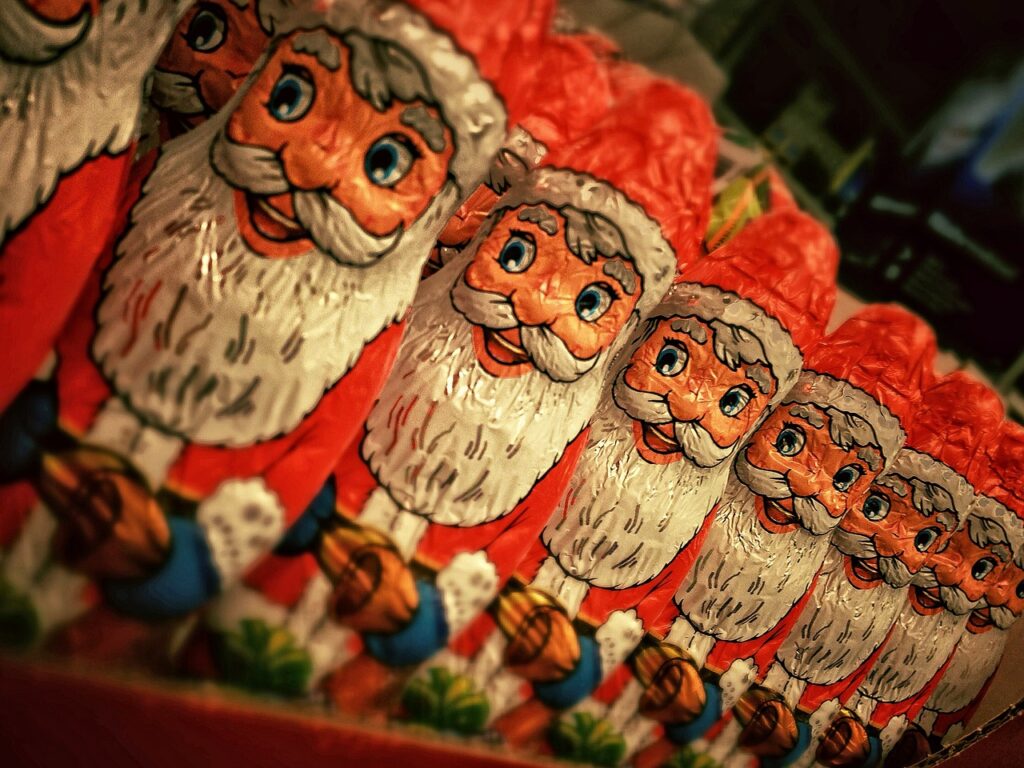 A row of foil-wrapped chocolate Santa Claus figures, each with a jolly smile, red hat, and white beard, displayed closely together on a shelf.