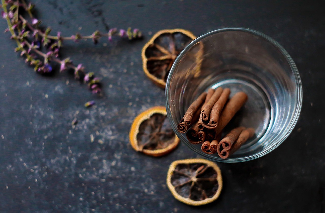 Glass with cinnamon sticks, dried orange slices, and sprigs of lavender on a dark surface.