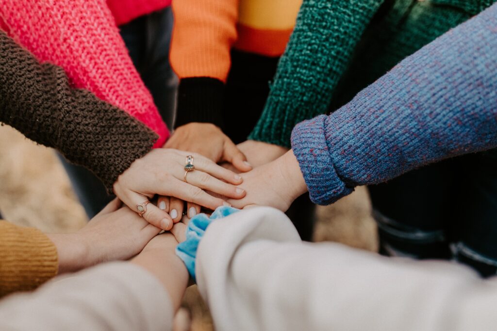 Circle of women in colorful sweaters touching hands in the middle
