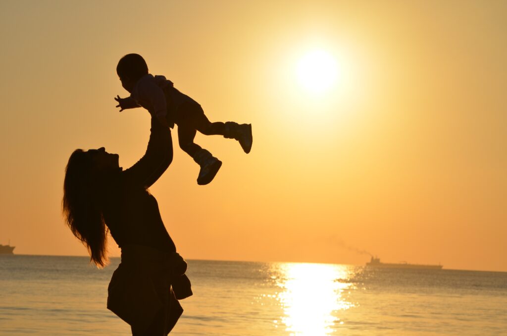 mother and baby in silhouette on beach at sunset