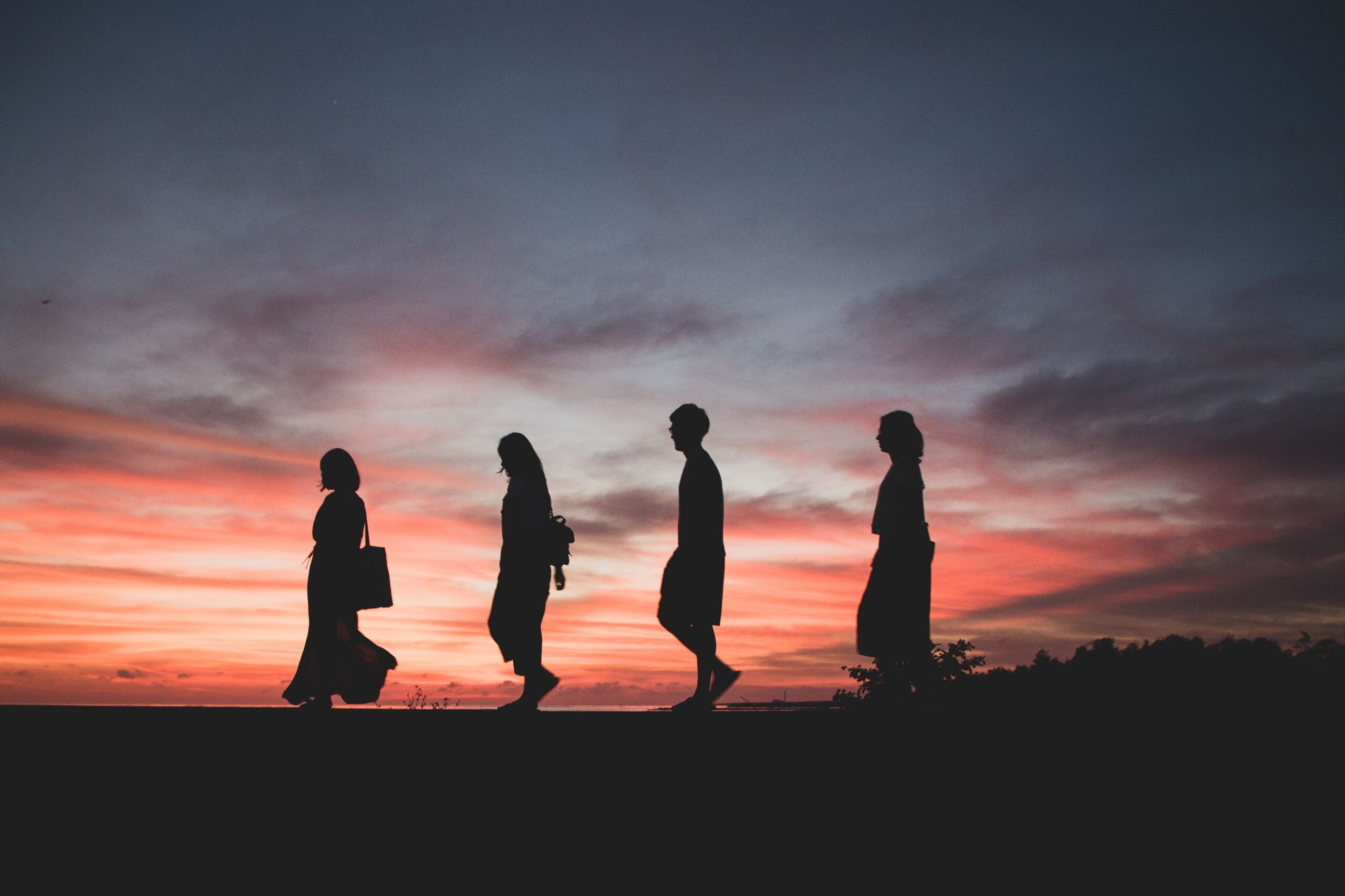 Four people in profile walking with the sunset behind them