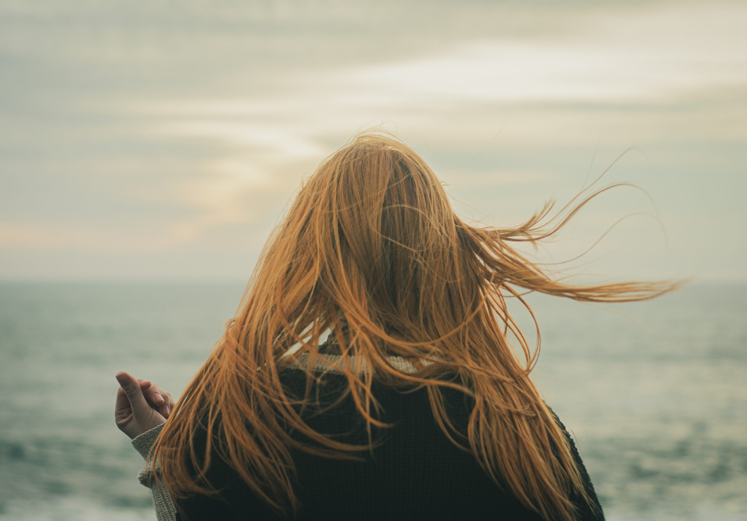 red haired teenaged girl facing the ocean