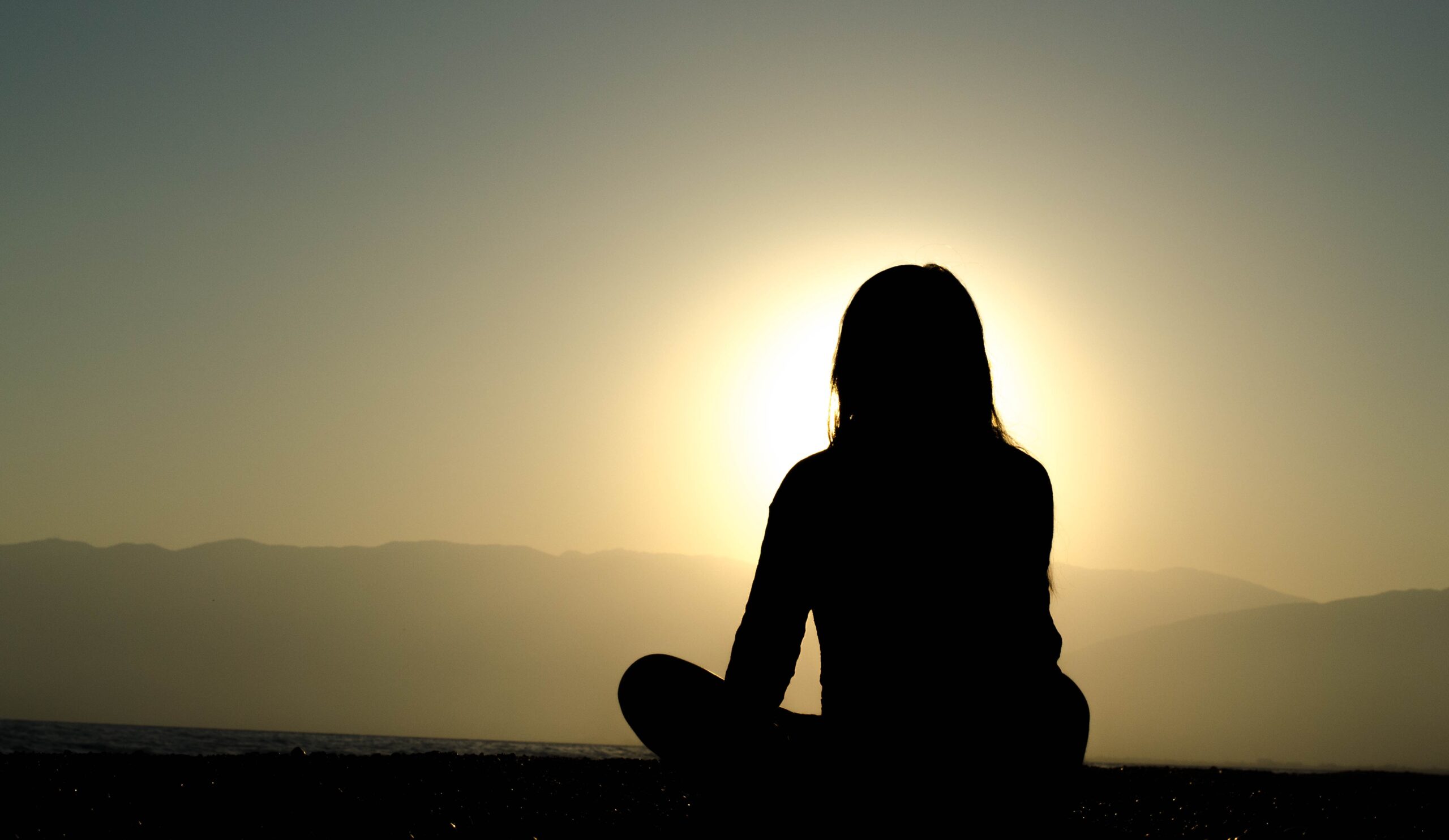 silhouette of a woman photographed from behind in the lotus position facing the sunrise