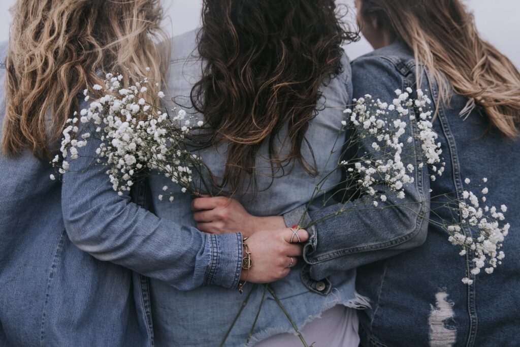 three women embracing, shot from behind, two holding sprigs of babys breath