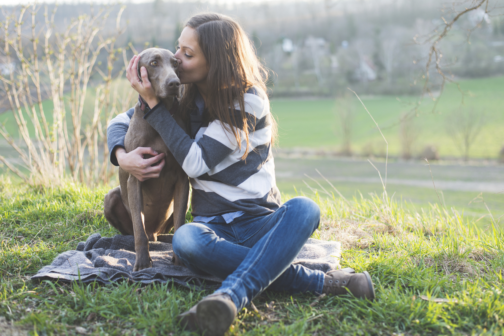 woman in sunlit field hugging her dog and giving it a kiss on the head