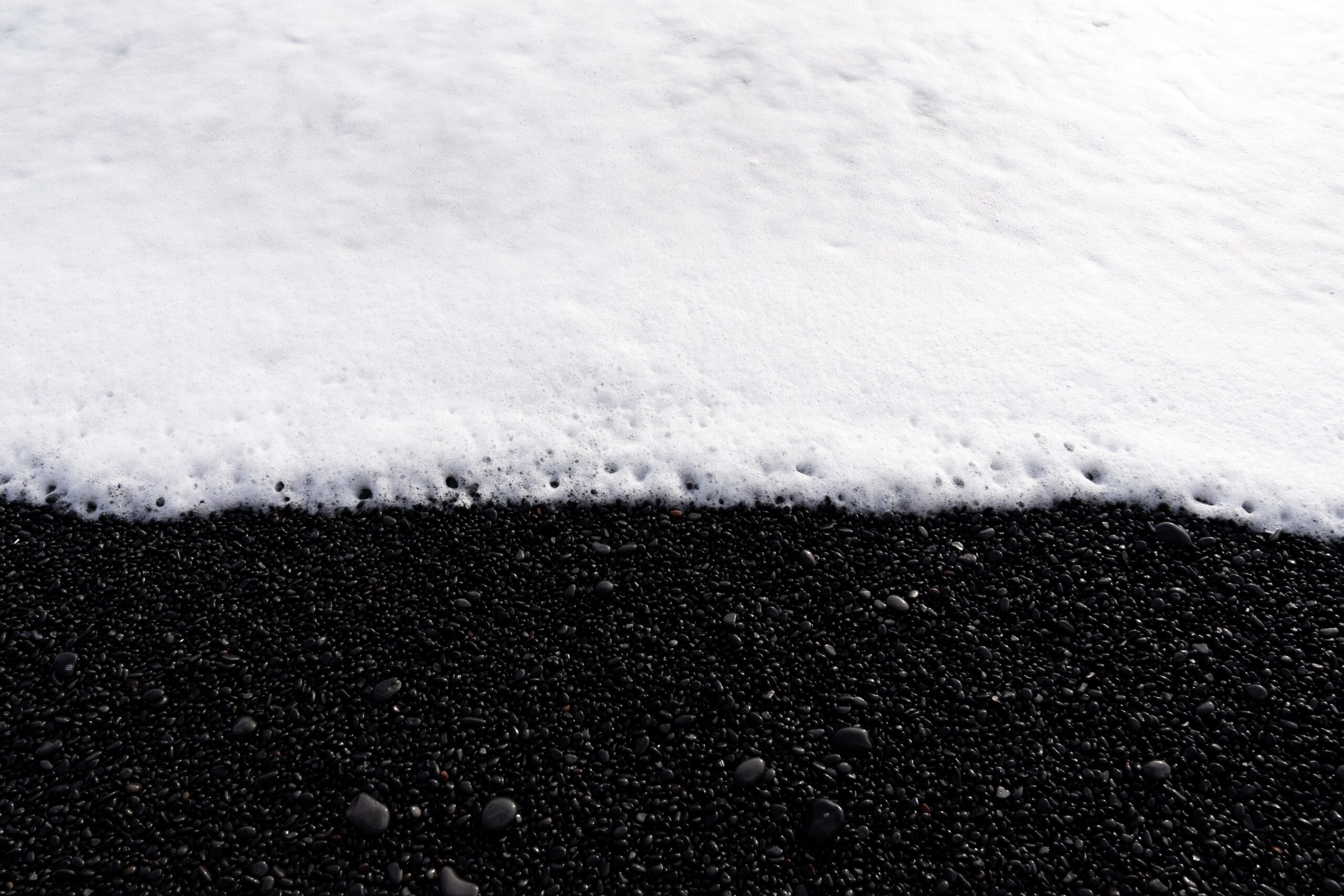 Wave foam gently laps against black pebbles on a beach.