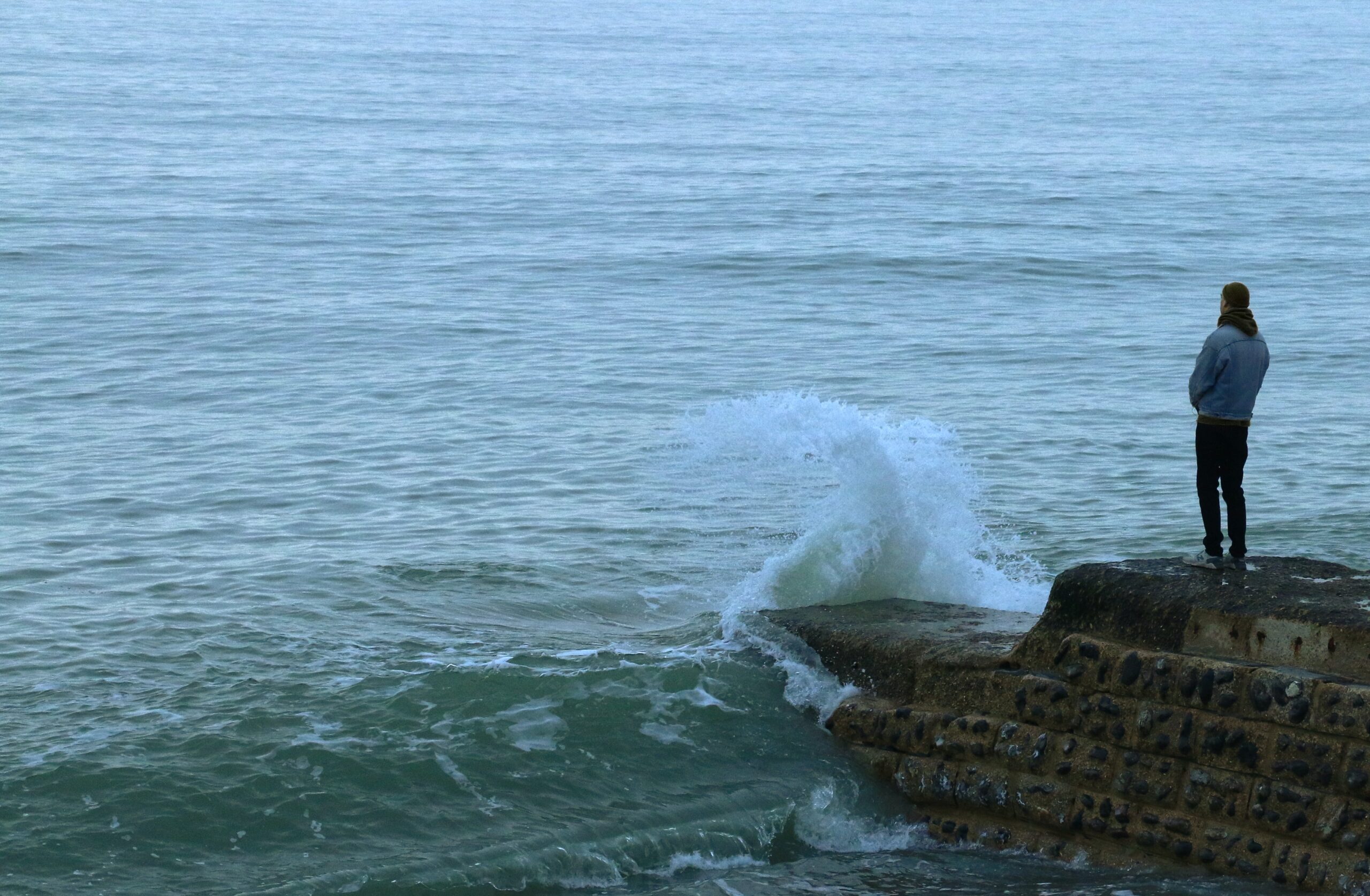 man standing on rocks looking at waves in water