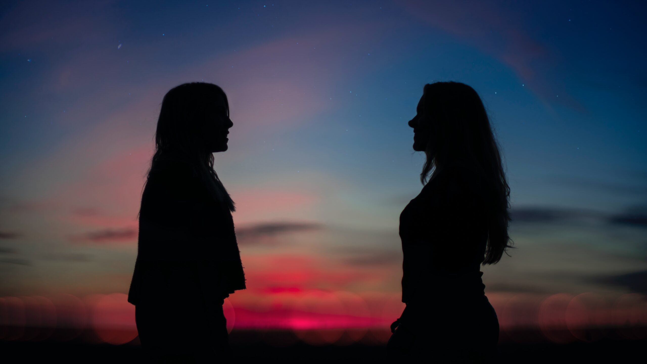 two women facing each other in profile, silhouetted against a sunset