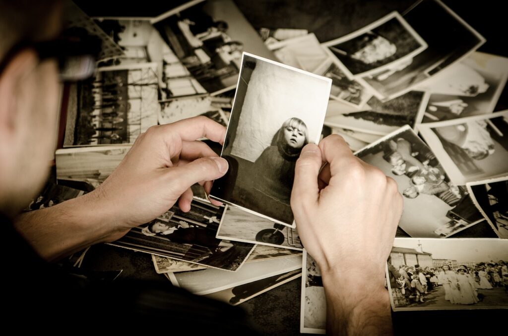 someone's hands are holding a black and white photo of a child, underneath is a pile of photos