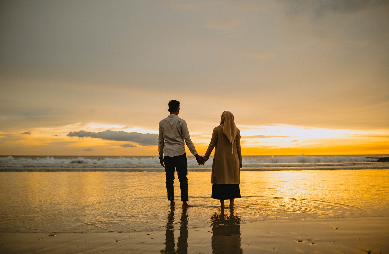 a couple holds hands on a beach during a sunset