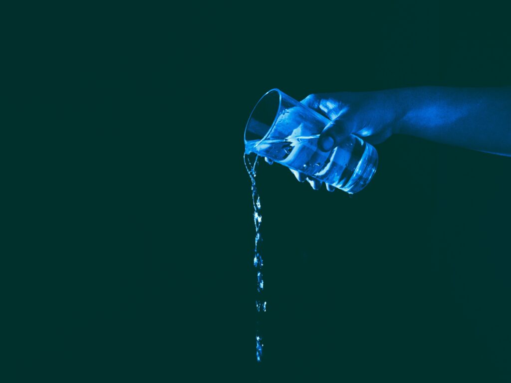 hand pouring water from a glass lit by blue light