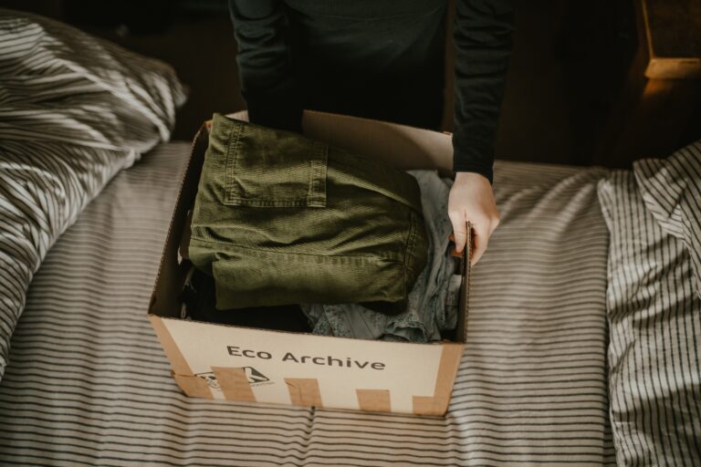 man putting a box of clothes on top of a bed with striped sheets