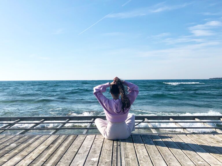 teenaged girl in sweats sitting on a pier staring at the ocean