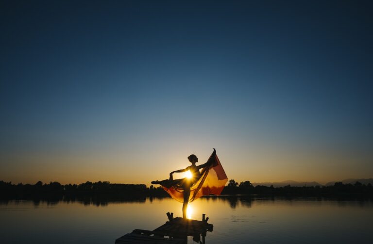 silhouette of a ballet dancer in arabesque position against a dark blue sunset