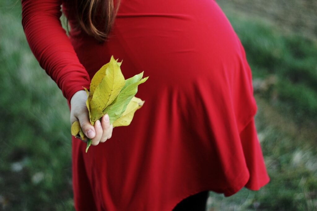 pregnant woman in red dress holding leaves