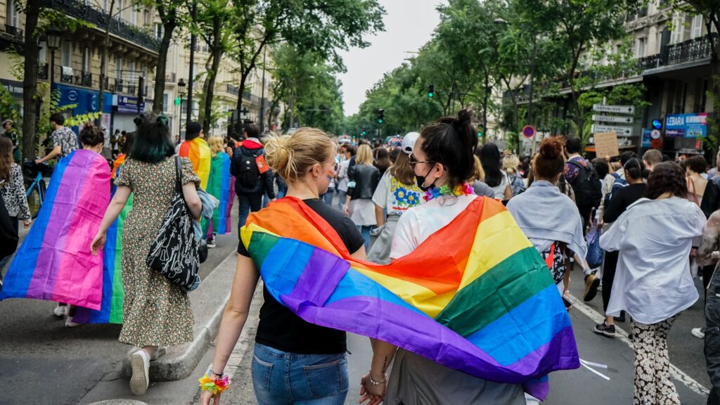 two women wrapped in a pride flag walking in a pride parade