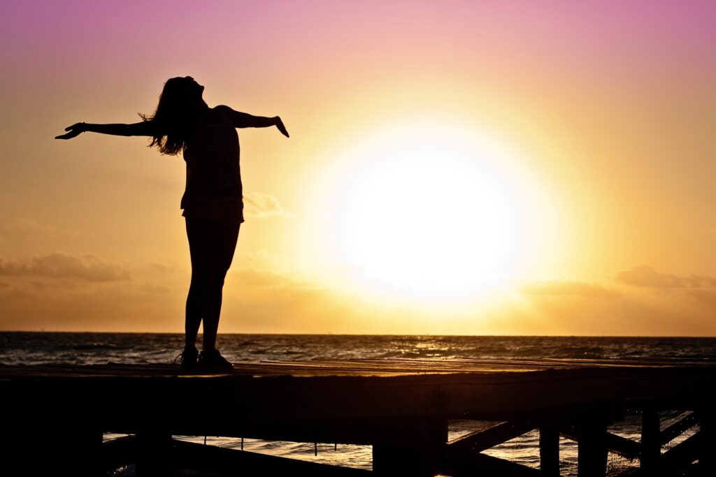 woman with outstretched arms on a pier at sunrise