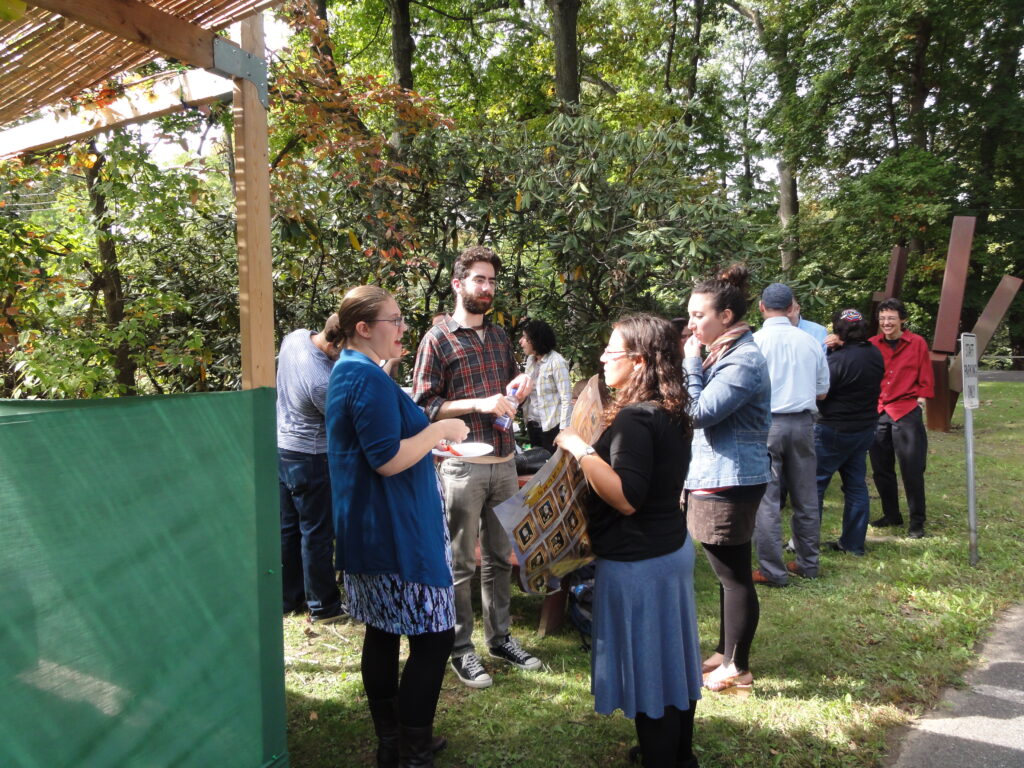 group of people standing around and chatting outside a sukkah