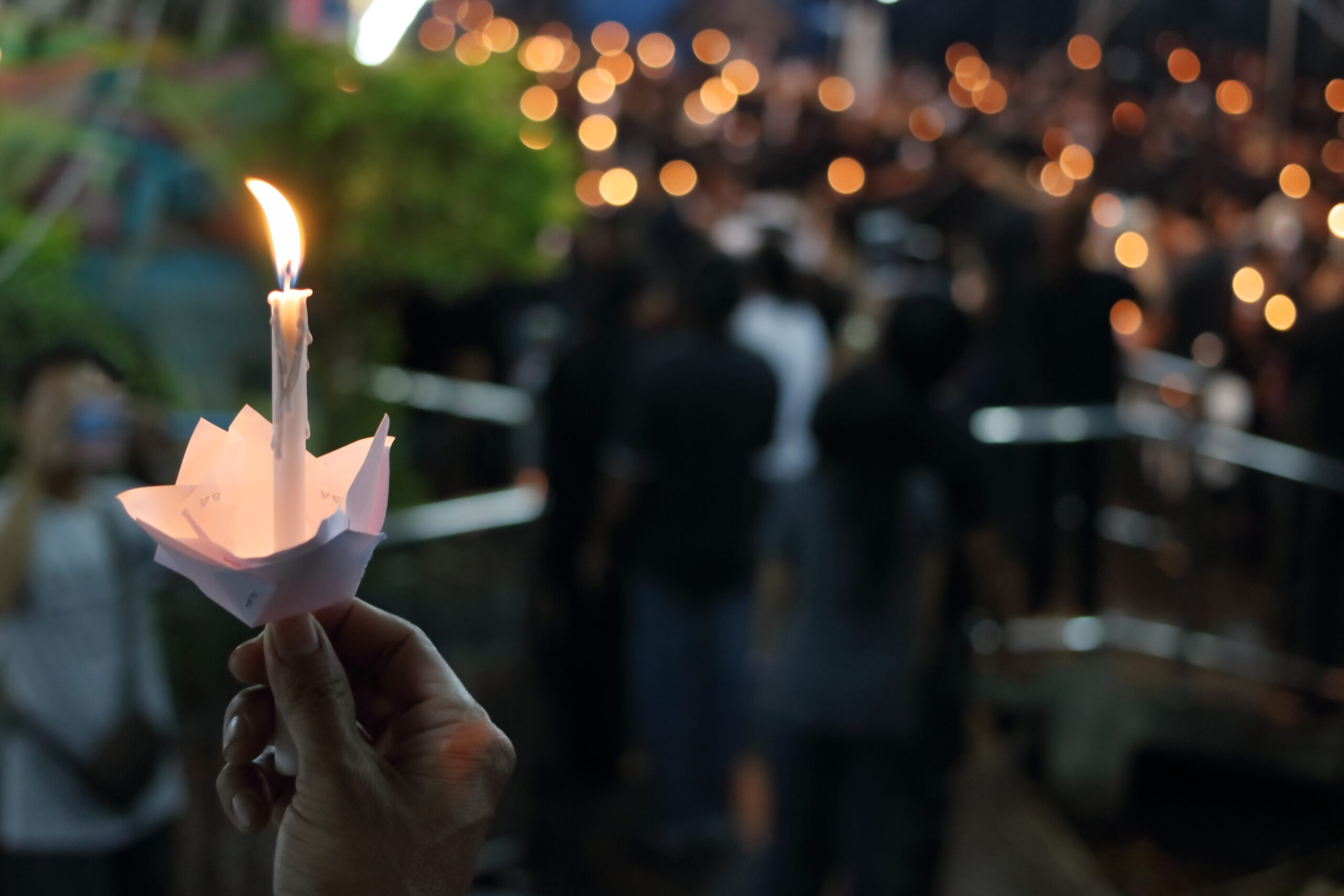 close up of hand holding candle - crowd in the background holding many candles