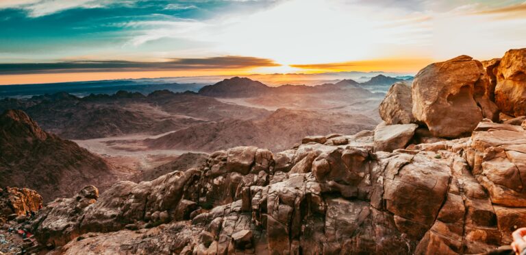 Mt. Sinai, a rocky mountain landscape at sunrise with a dramatic sky and distant peaks.