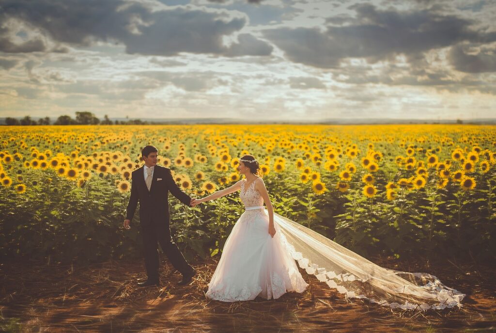 a groom and bride hold hands by a field of sunflowers