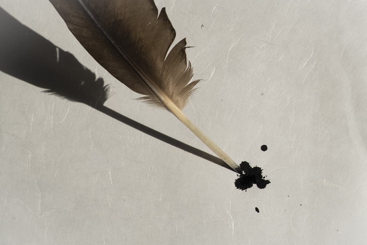 a feather drops black ink onto a blank page