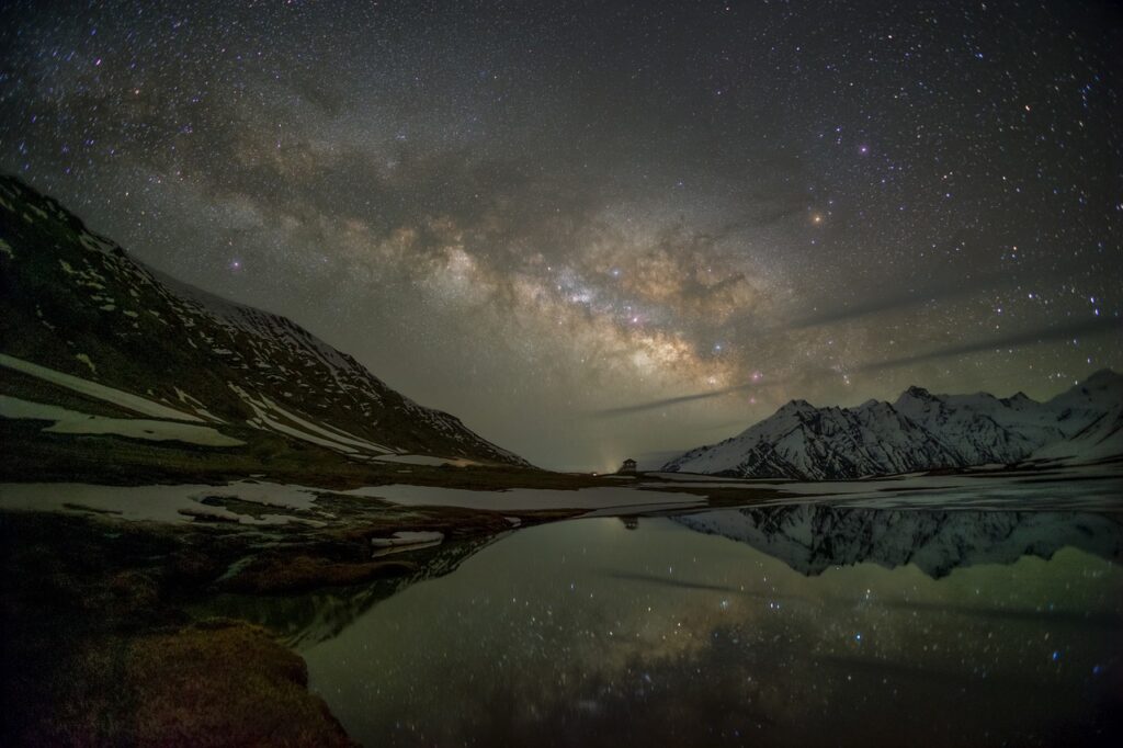 dark cloudy and starry sky overlooks a body of water surrounded by mountains