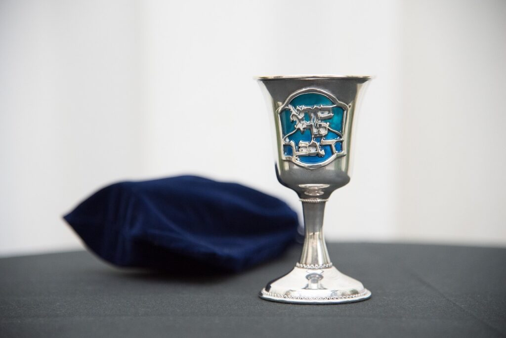 A silver kiddush cup with a blue design beside a folded dark blue cloth on a table.