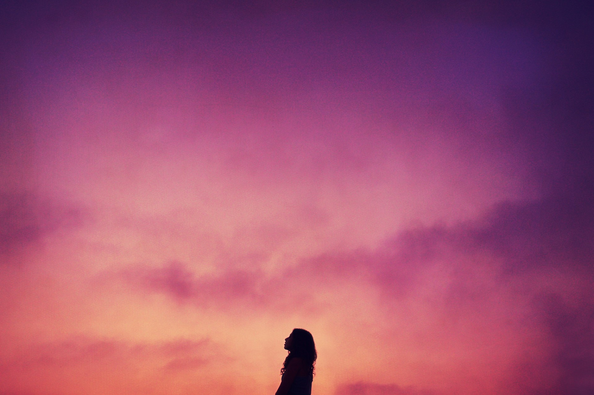 silhouette of a person looking up at a pink cloudy sky