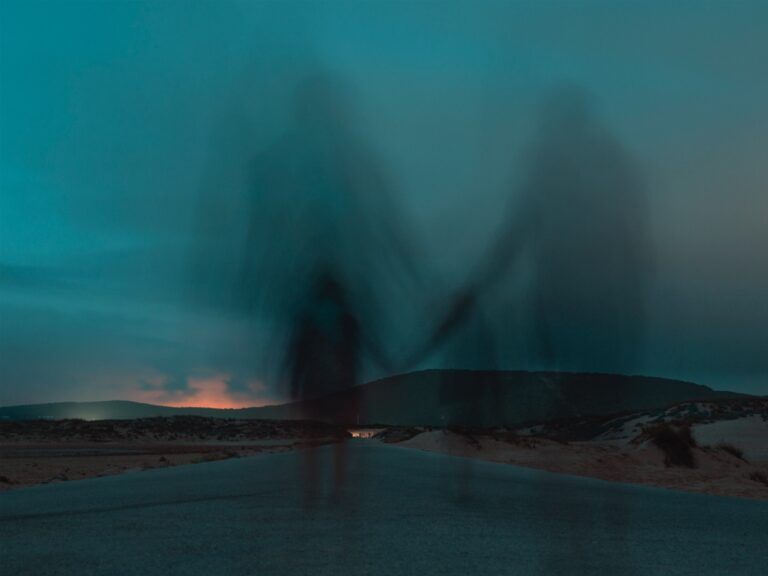 shadows-holding-hands-walking-on-dark-desert-road-toward-mountains