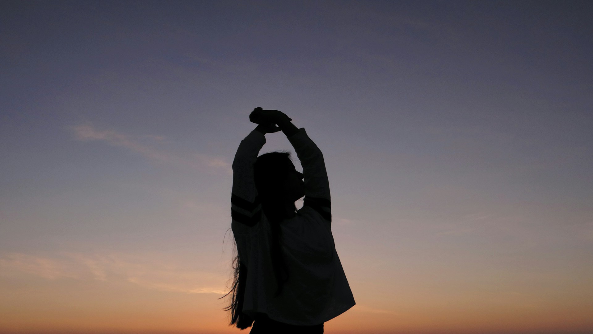 silhouette of a person clasping their hands above their head against a sunset