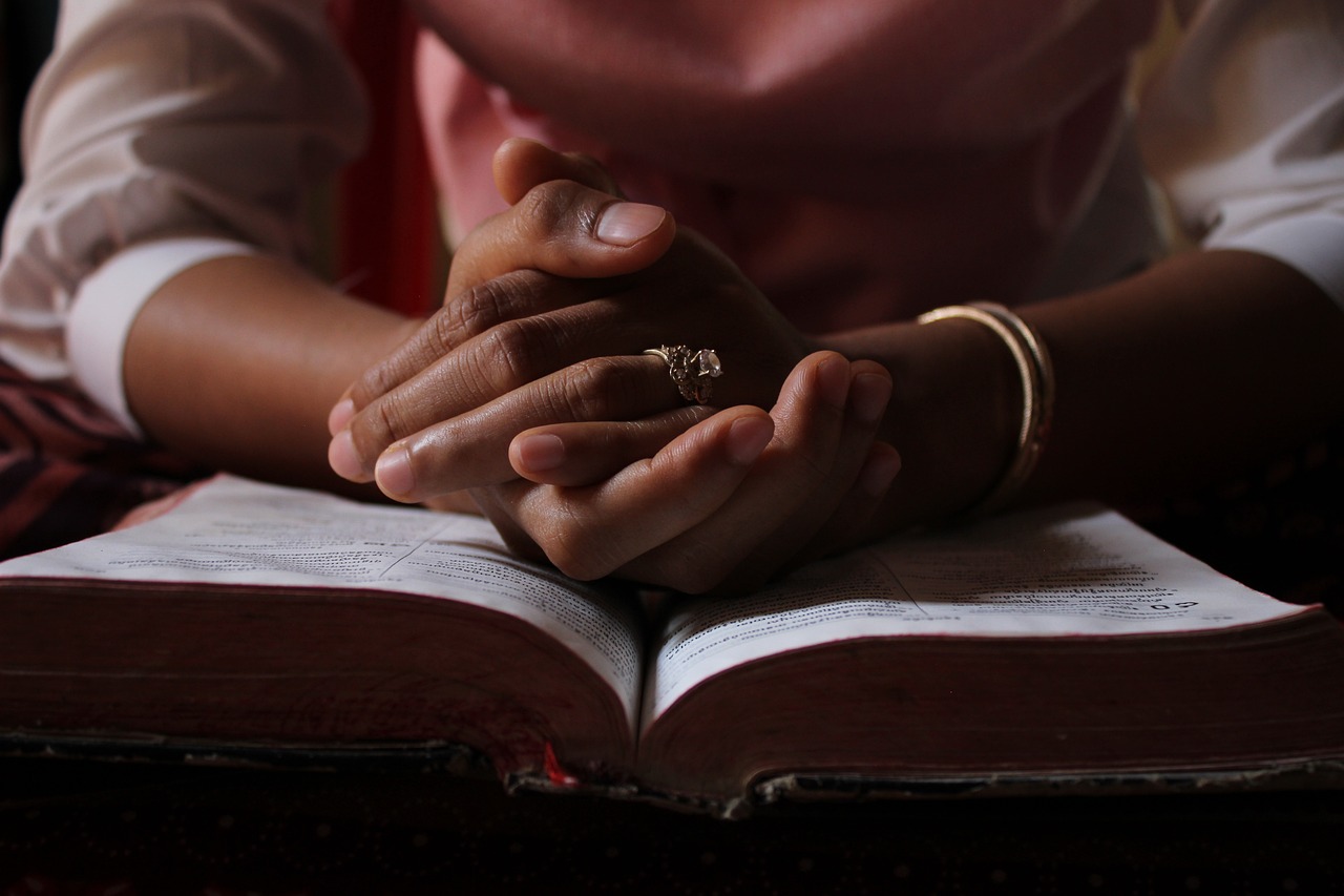 a person rests their clasped hands on an open book