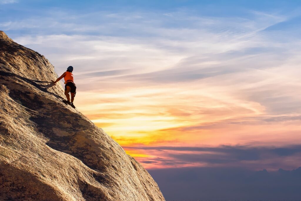 a mountain climber on a ledge with the sun peeking over the horizon