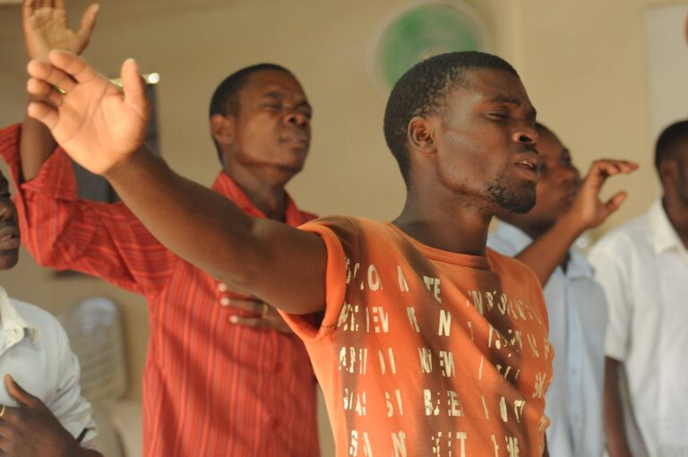 two people stand with eyes closed and arms outstretched, others are blurry in the background