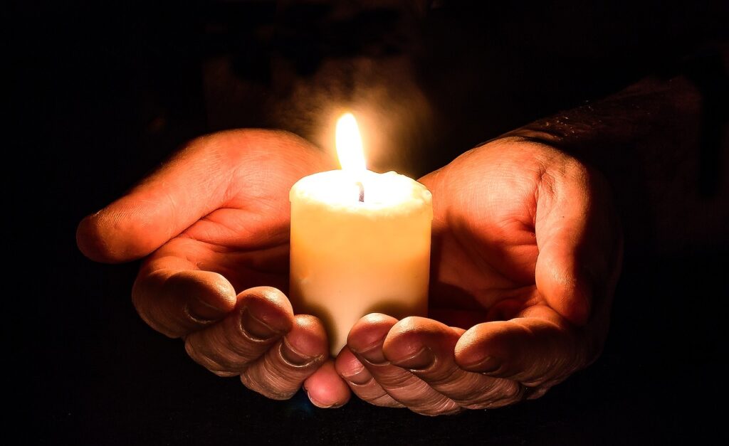 a person's hands are cupping a lit candle