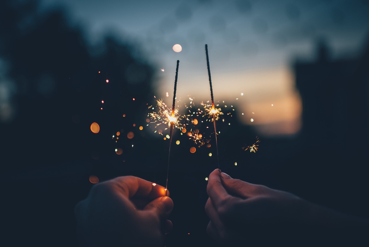 two hands holding burning sparklers next to each other