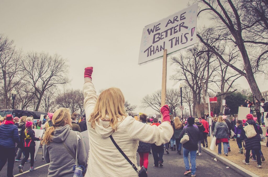 a protest with a person holding up a fist and in the other hand a sign that says "WE ARE BETTER THAN THIS"