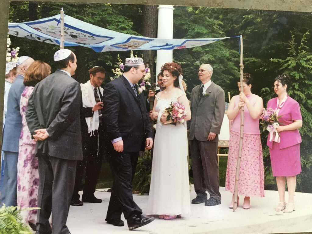 a couple stand under a chuppah surrounded by family and friends