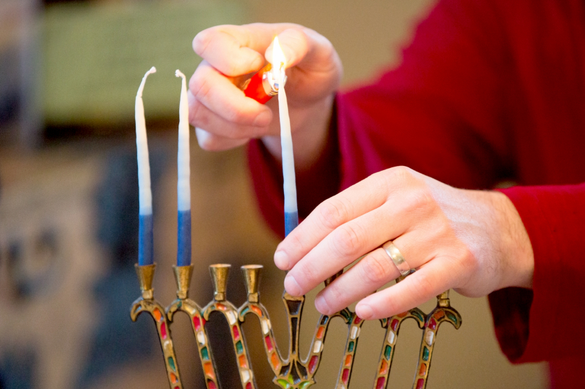 Person lighting a Hanukkah menorah with blue and white candles.