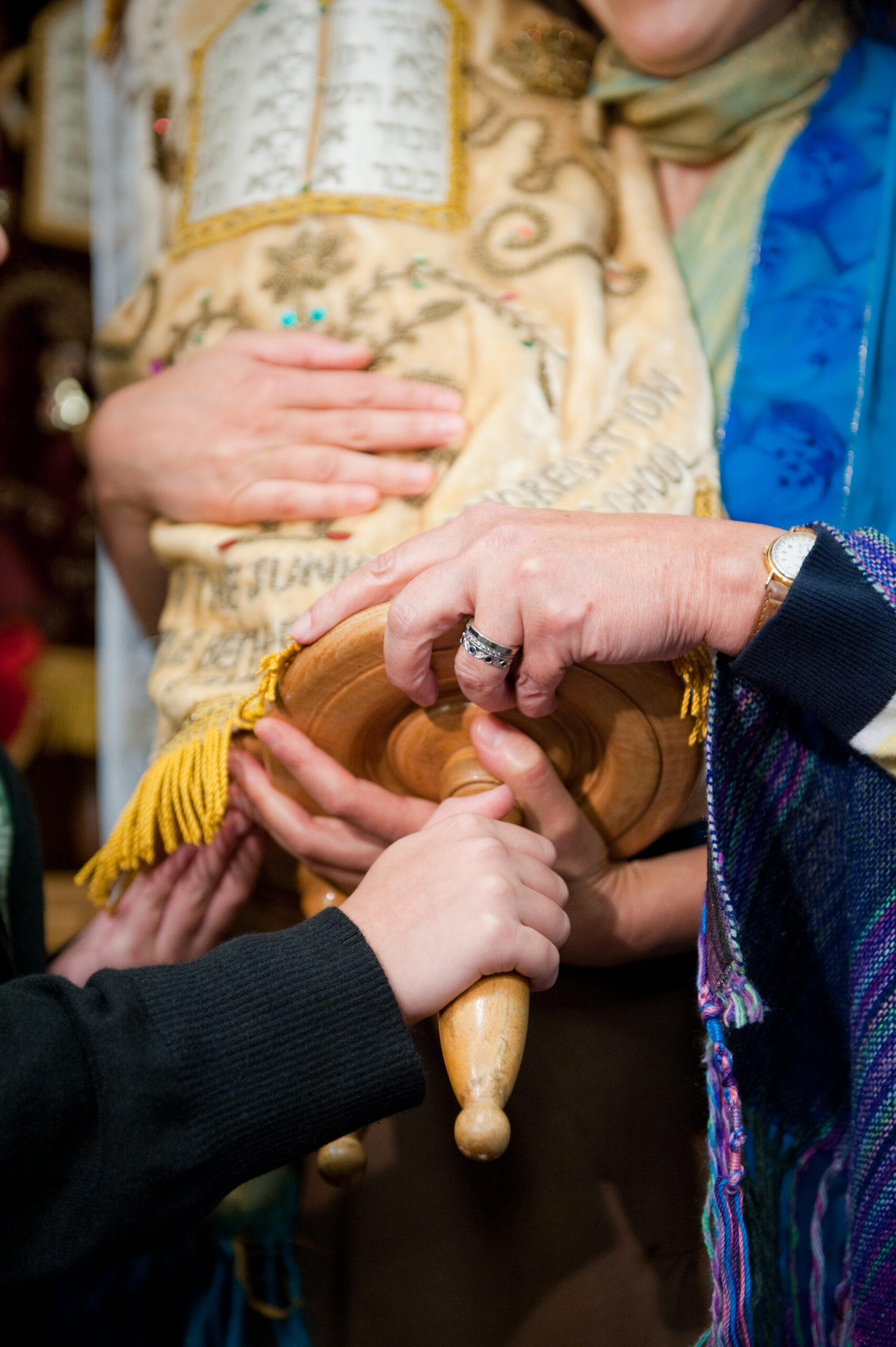 Hands holding a Torah scroll wrapped in an ornate cover during a Jewish ceremony.