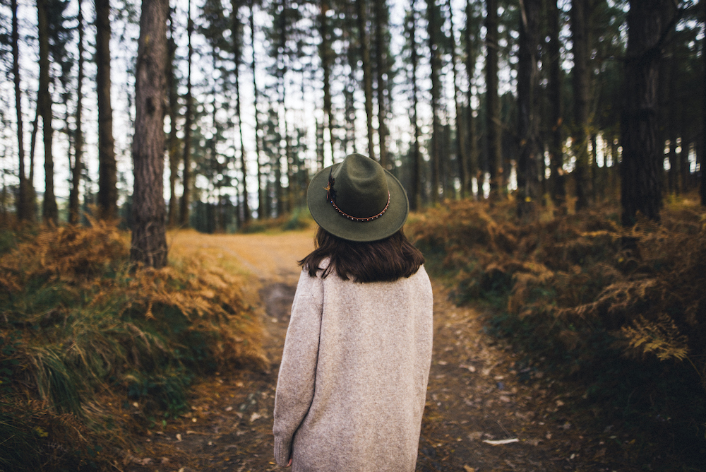 a person with medium length hair and a hat is walking on a path in the forest