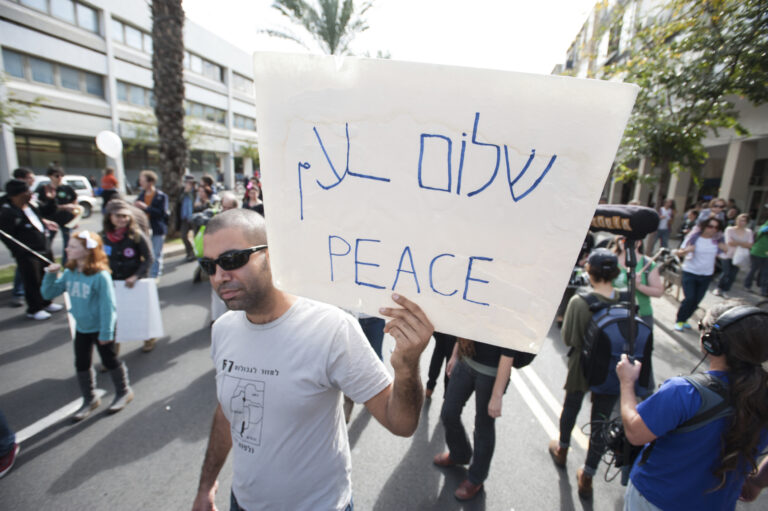 an activist holds a sign that says Shalom and Salaam