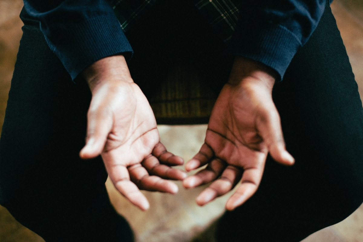 Close-up of a person sitting with hands open and resting on their knees, palms facing upward.