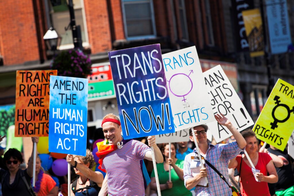 People at a trans rights rally holding colorful signs advocating for equality and human rights.