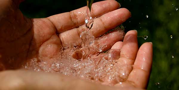 Water pouring into cupped hands, with droplets splashing and glistening in the light.