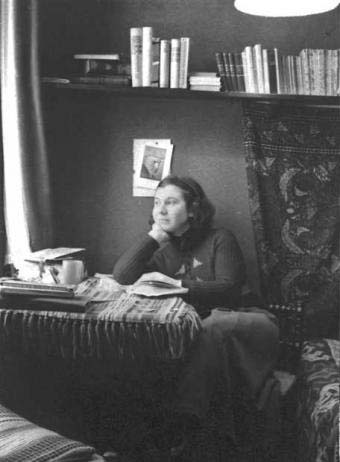 A person sitting at a desk, looking thoughtful, surrounded by books and papers, in a cozy room with a tapestry.