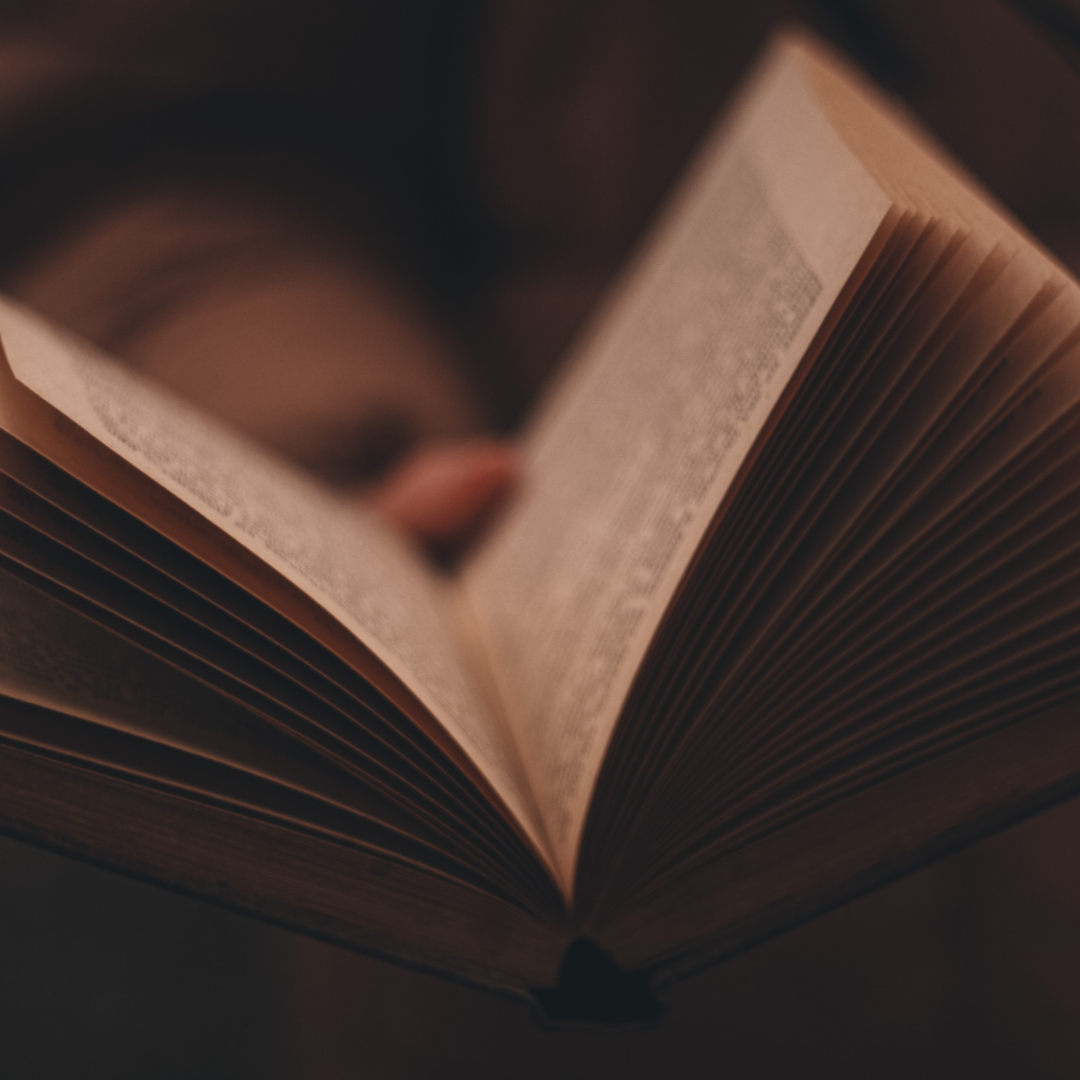 Close-up of an open book with visible pages, held by a persons hand against a dark blurred background.