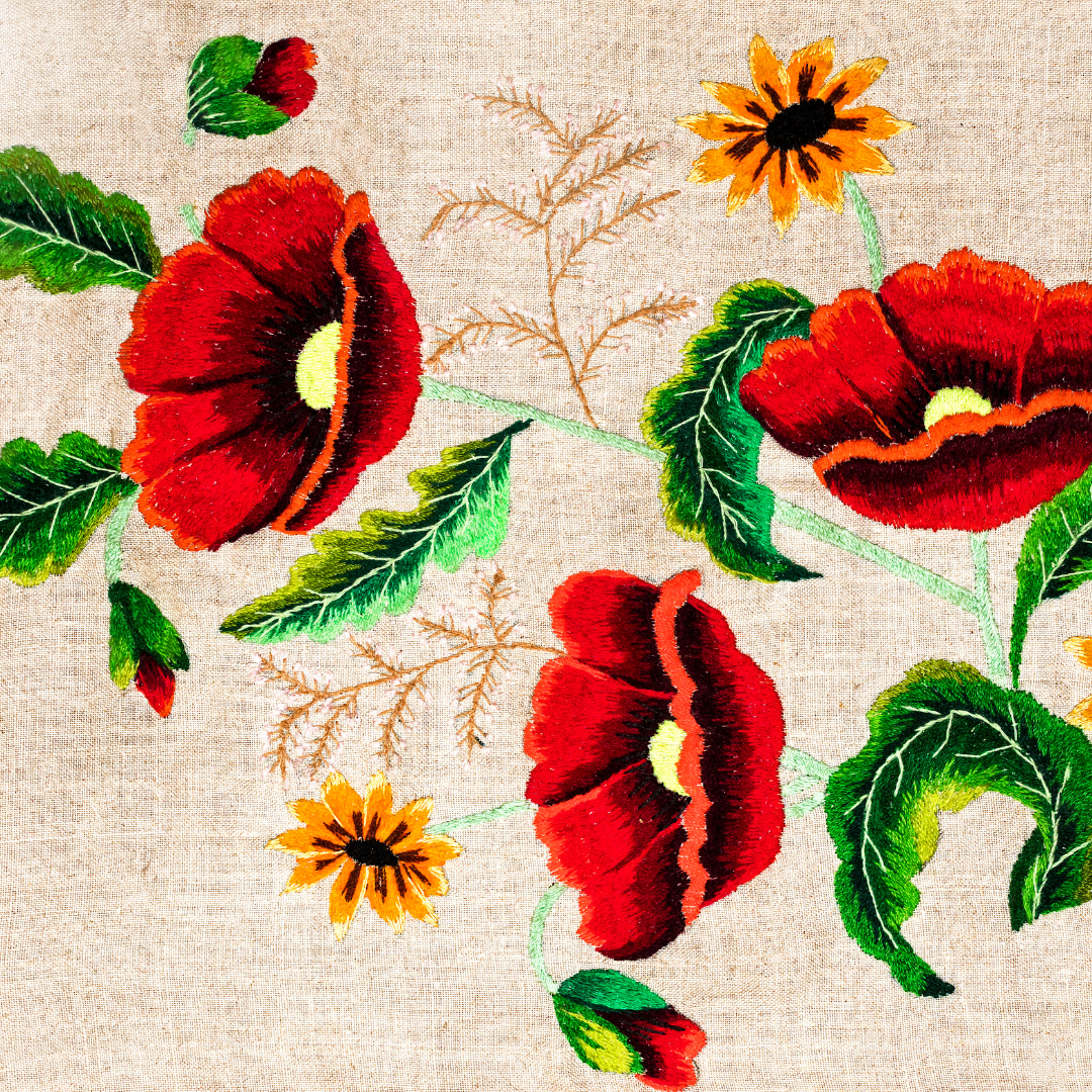 Embroidered red poppies and sunflowers on beige fabric with green leaves and stems.